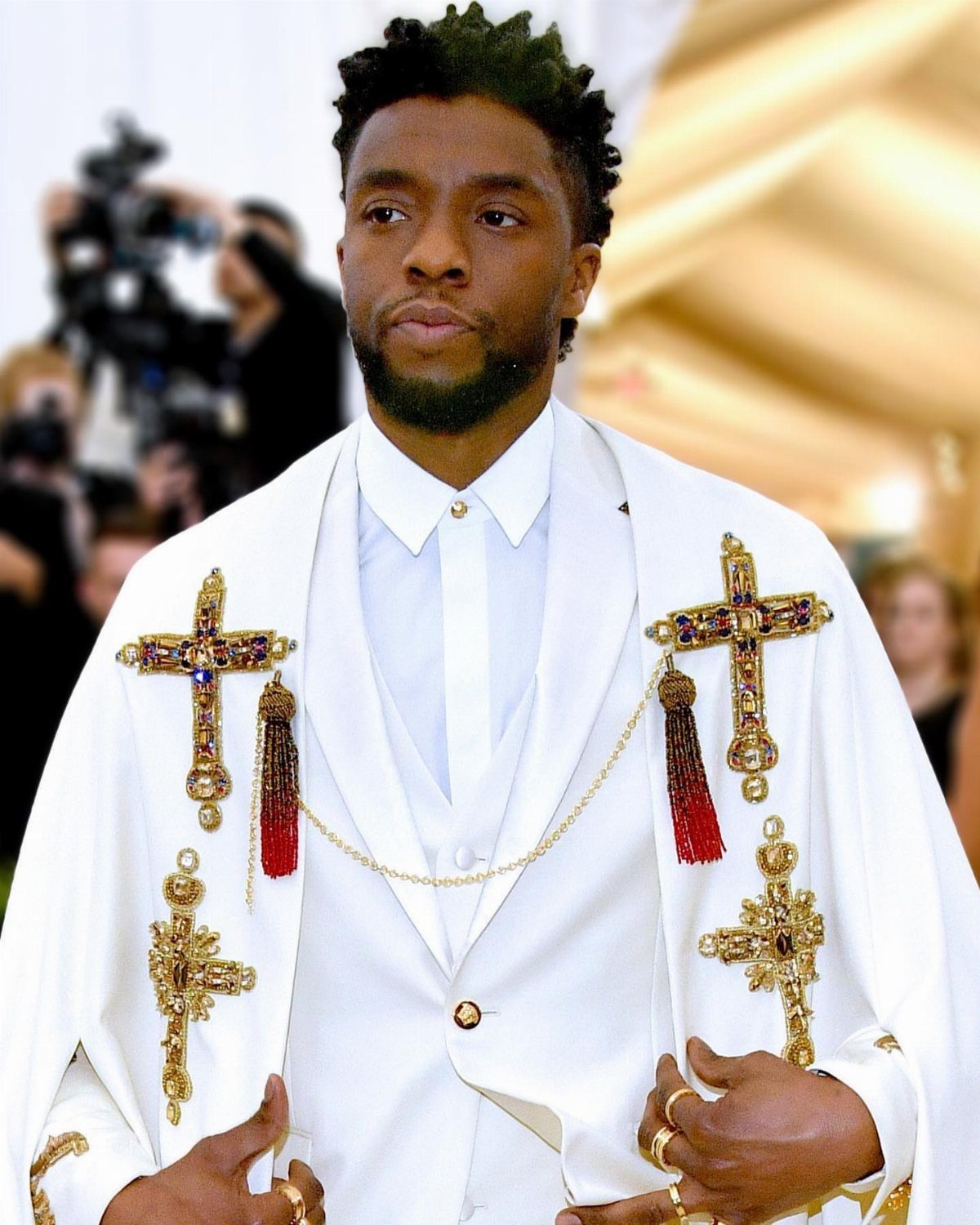 Chadwick Boseman in a white suit and cape with ornate gold jeweled crosses.