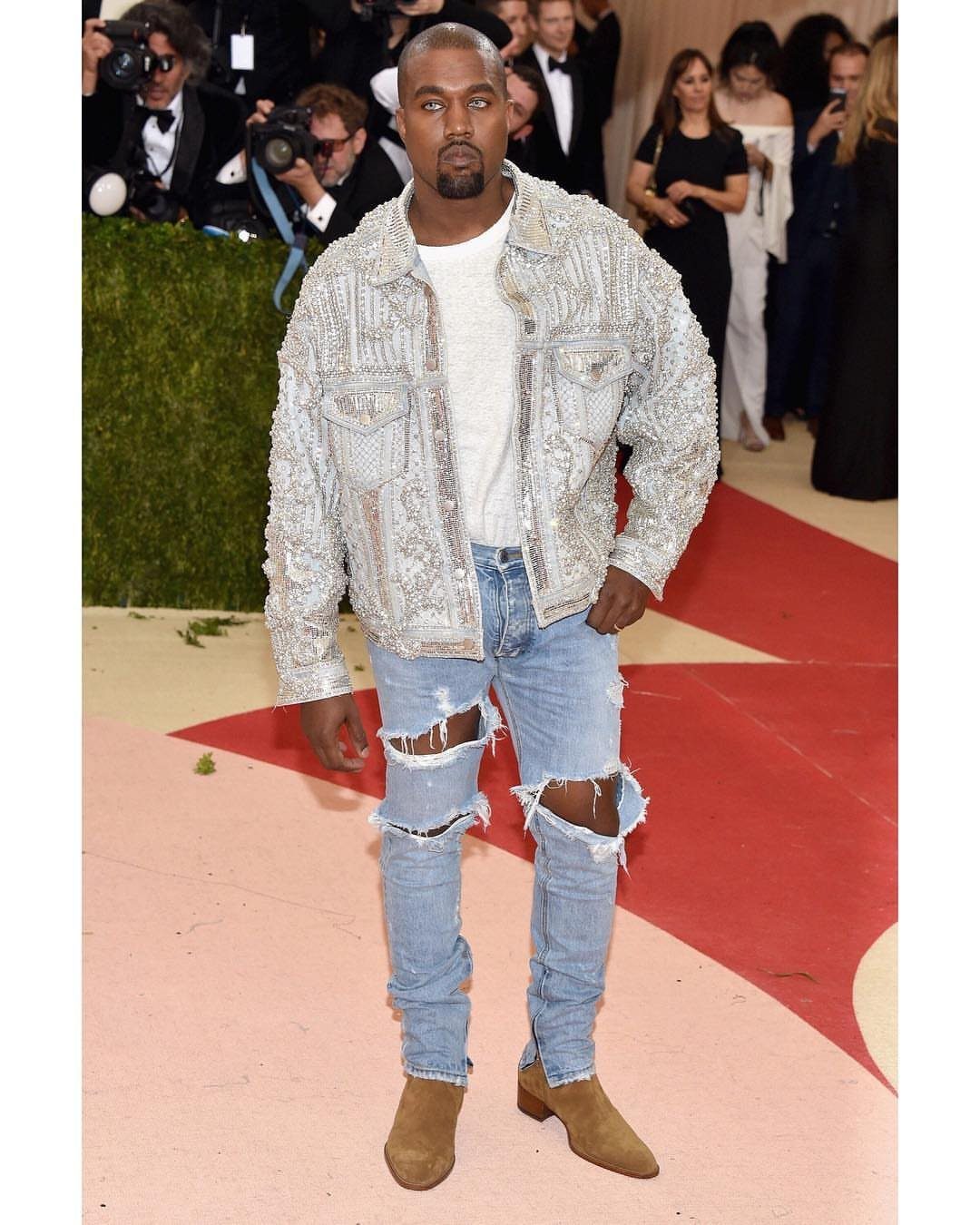 Kanye West wearing a silver metallic Balmain jacket and ripped blue jeans.