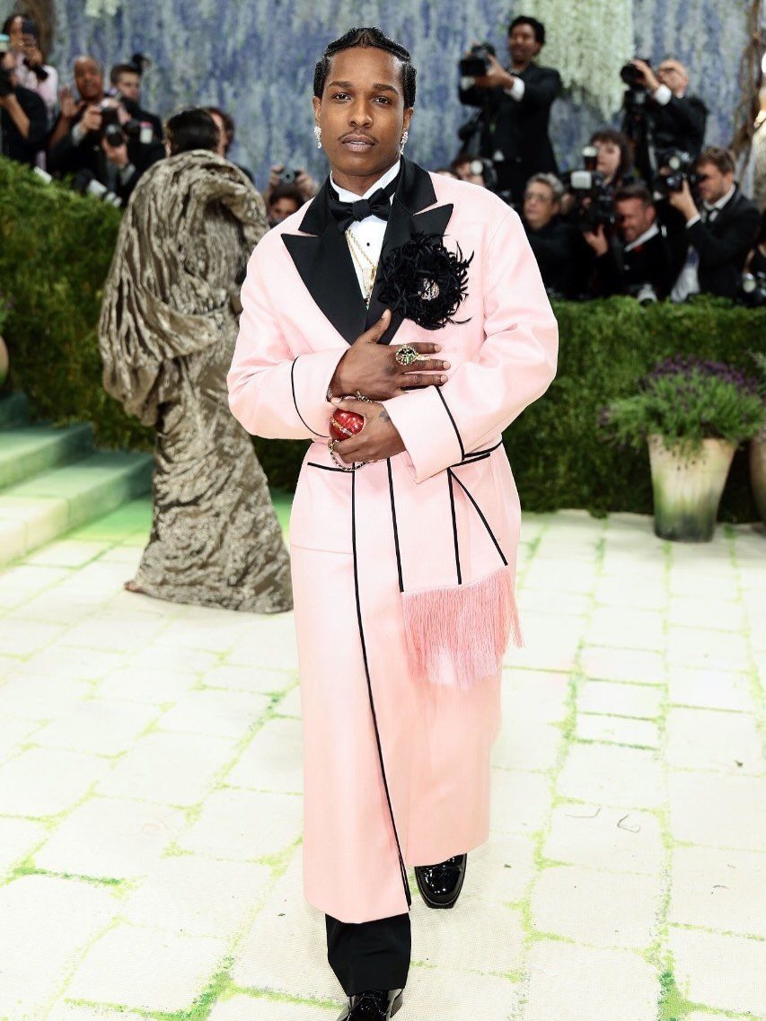 Man in a long light pink coat with black lapels posing at an event