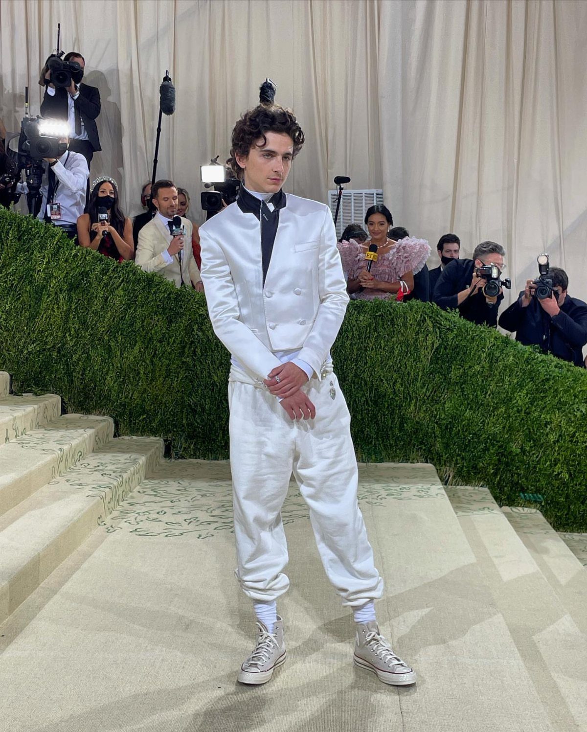 Timothée Chalamet wearing a white suit and white Converse sneakers on a staircase.
