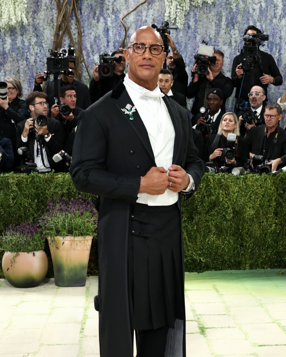 Man in a black tuxedo and kilt posing on a red carpet.