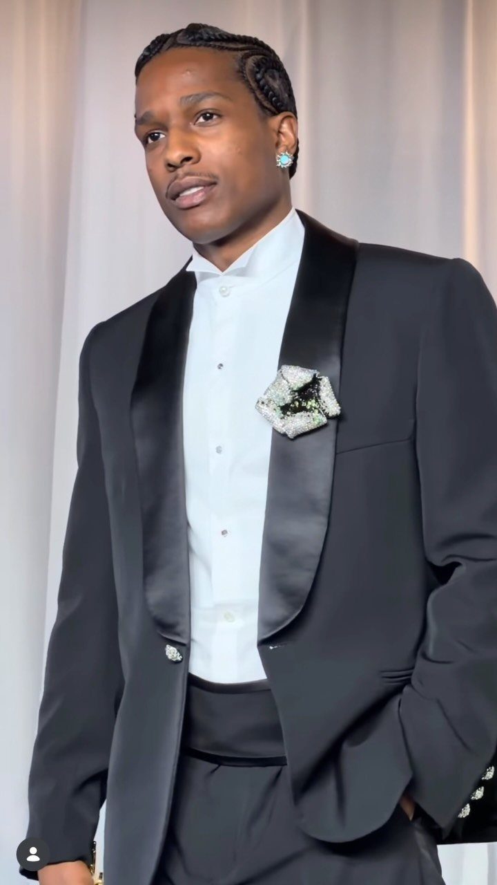 Man in a black tuxedo with a white shirt and decorative brooch.