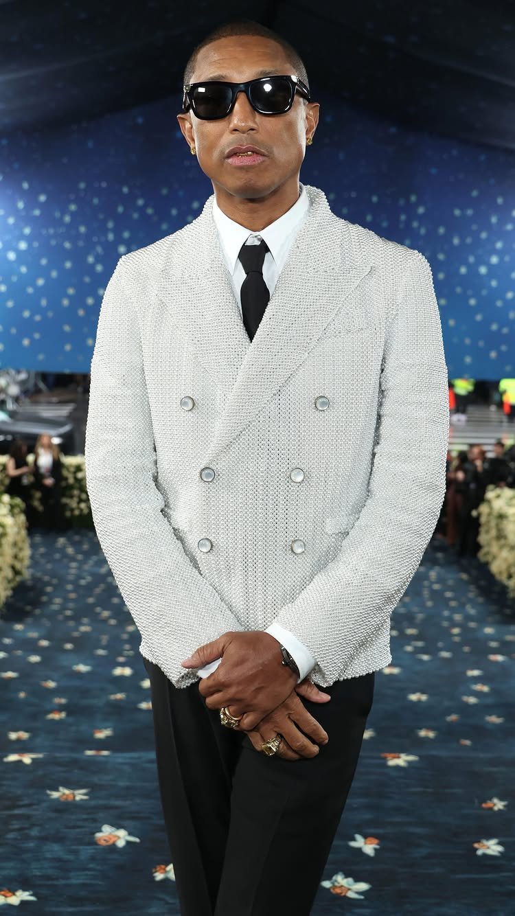Pharrell Williams in a white textured double-breasted blazer and black sunglasses at an event.