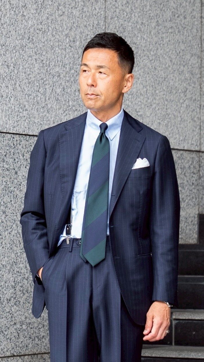 Man in a navy pinstripe suit with a striped tie and white pocket square.