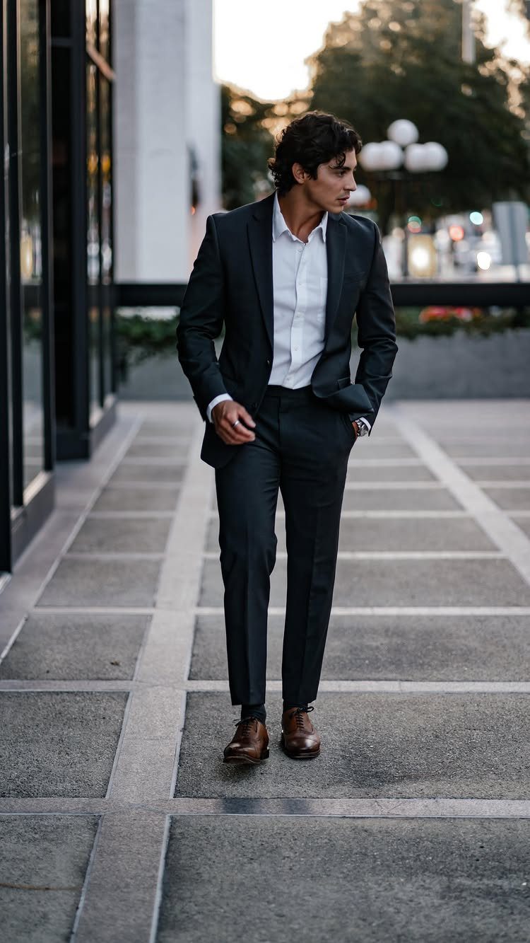 Man in a charcoal grey slim-fit suit and brown shoes on a city sidewalk