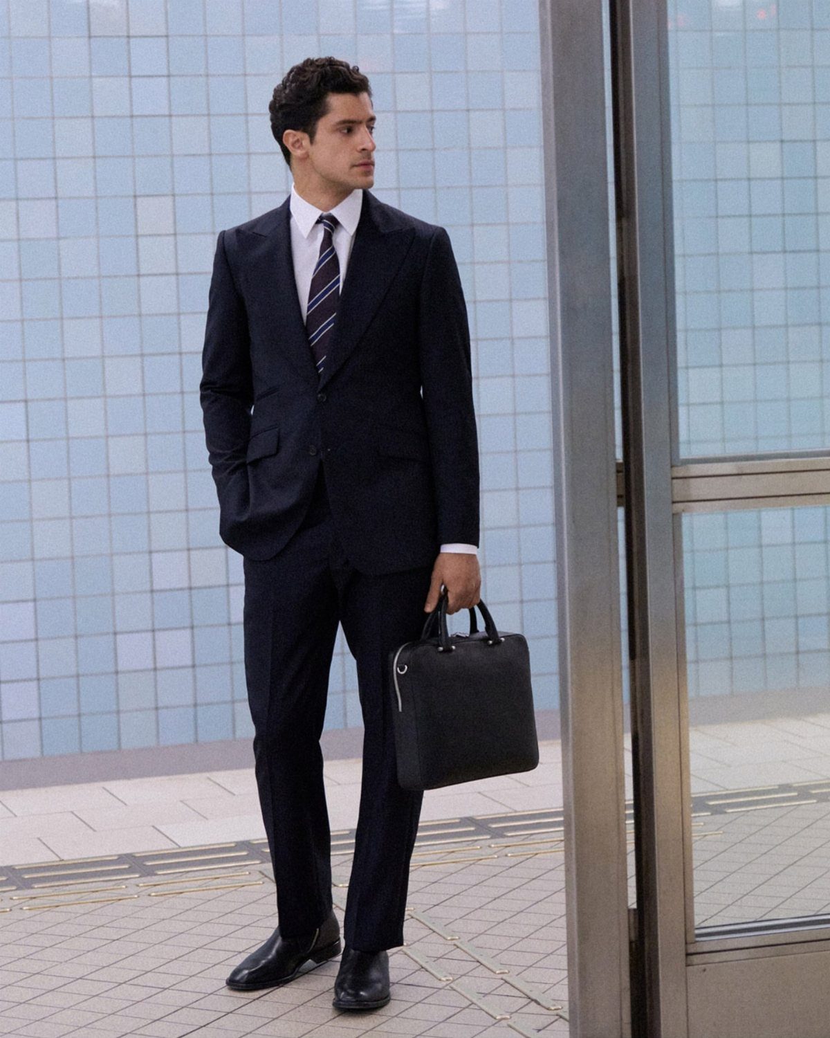 Man in a navy blue tailored business suit holding a black leather briefcase.