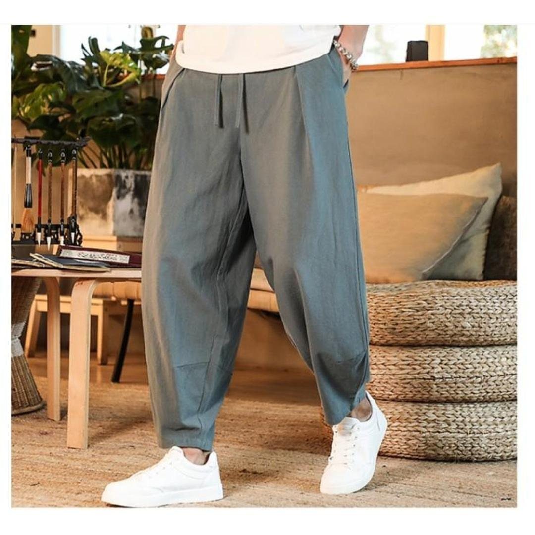 New Men's Fashion Pants: 12 Styles to Refresh Your Wardrobe 1 Grey-green linen drawstring pants paired with white sneakers in a bright interior.