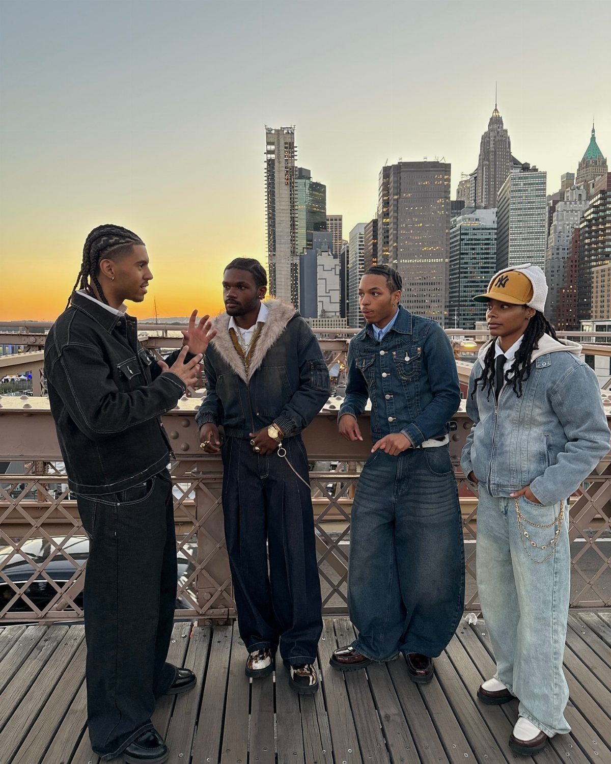 Four men in denim outfits standing on a bridge with New York City skyline background
