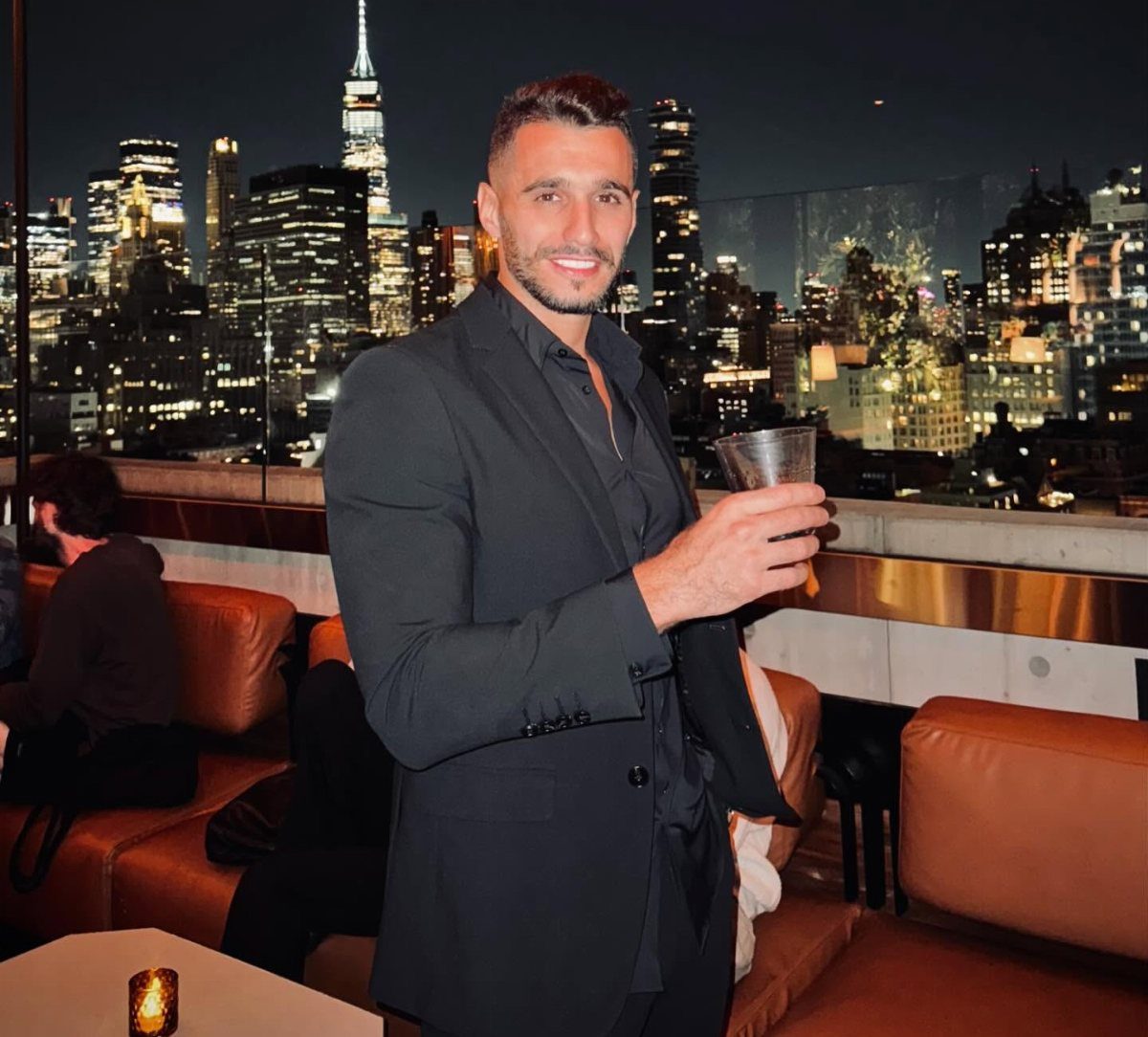 Man in black blazer and shirt posing on a New York City rooftop.