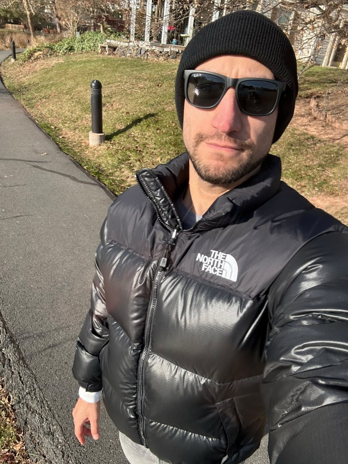Man wearing a black puffer jacket and black beanie on a sunny day.