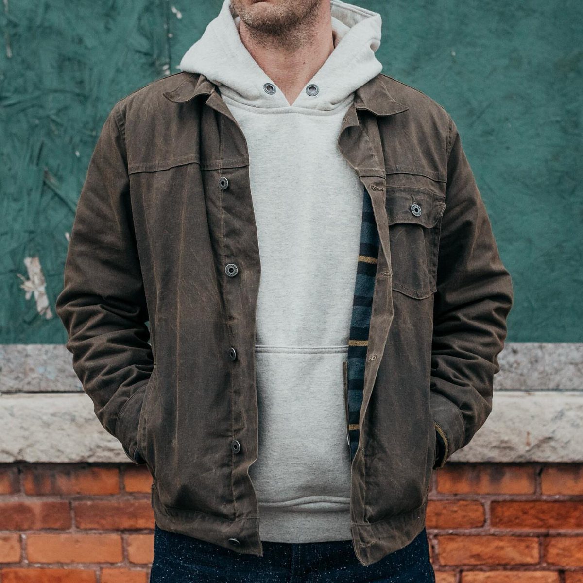 Man wearing a brown waxed canvas work jacket over a grey hoodie and jeans.