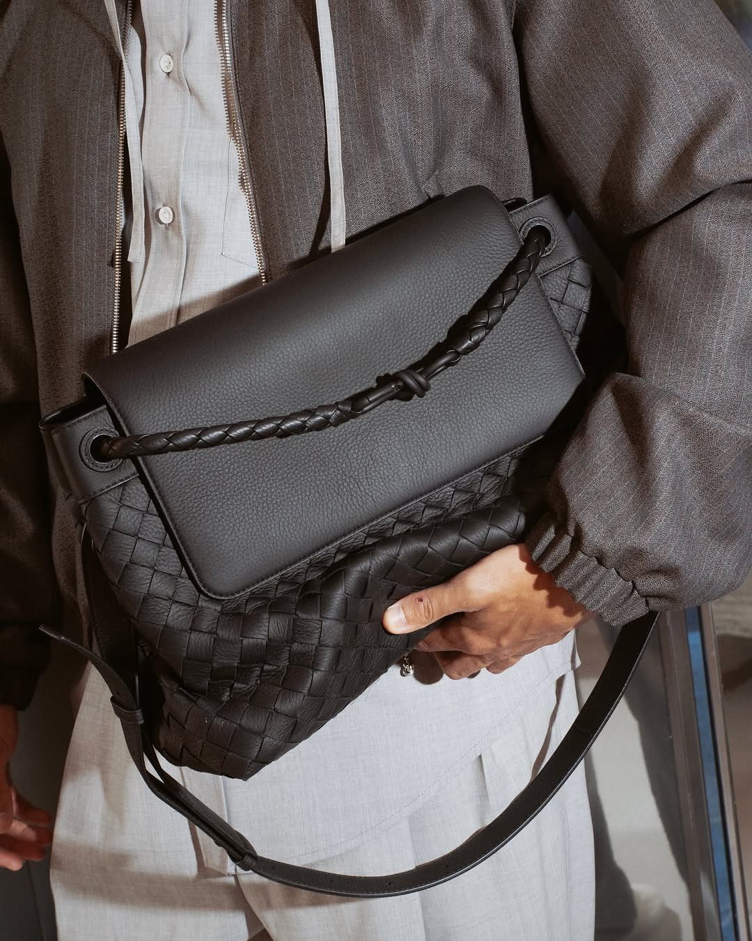 Black woven leather shoulder bag with a braided strap held by a person.