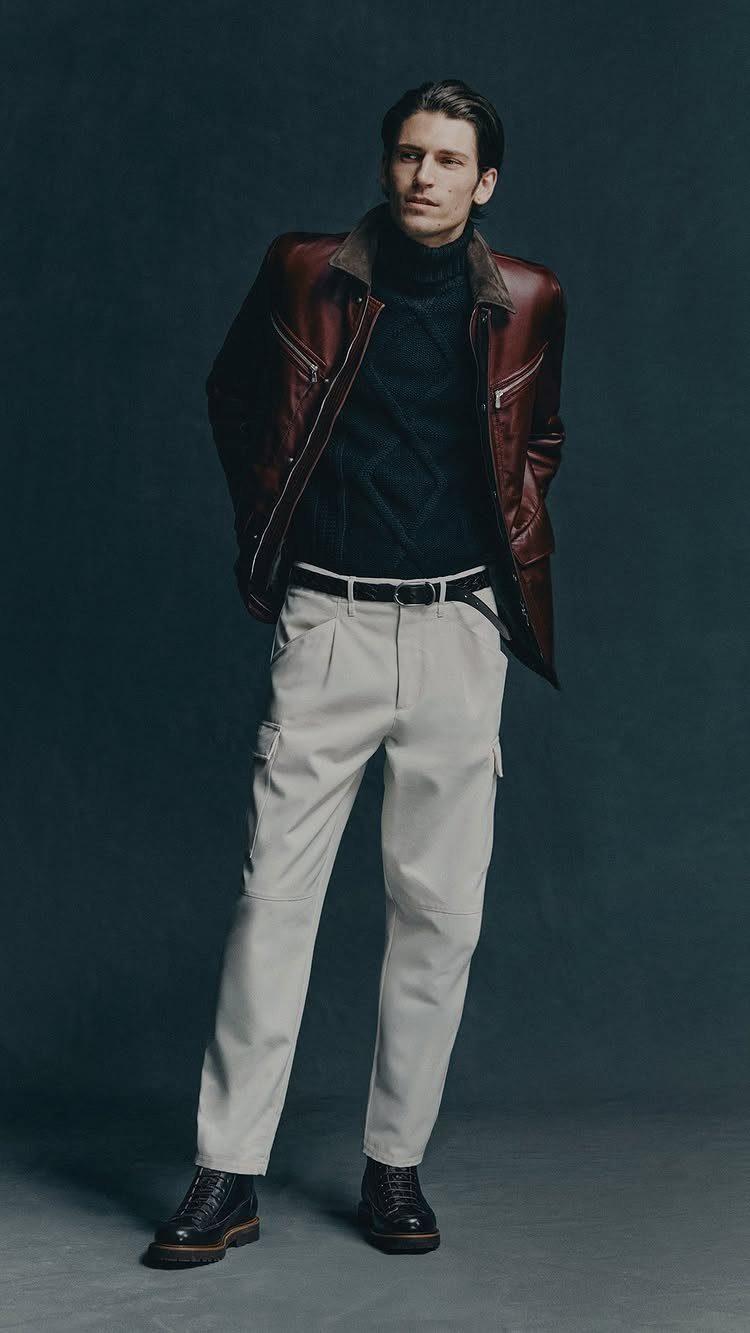 Man in a navy turtleneck, brown leather jacket, and off-white cargo trousers.