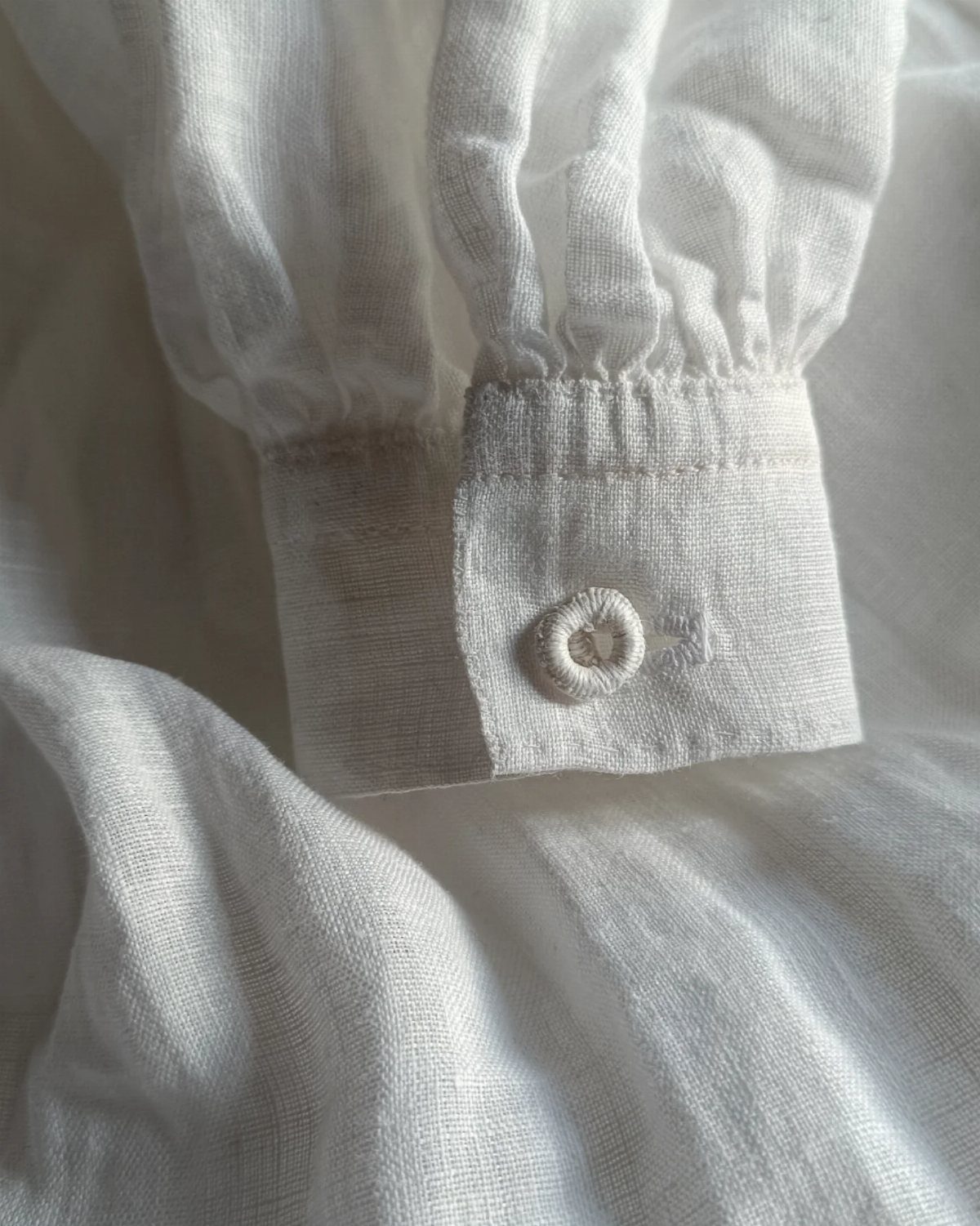 White linen shirt cuff with a button and gathered fabric sleeve.