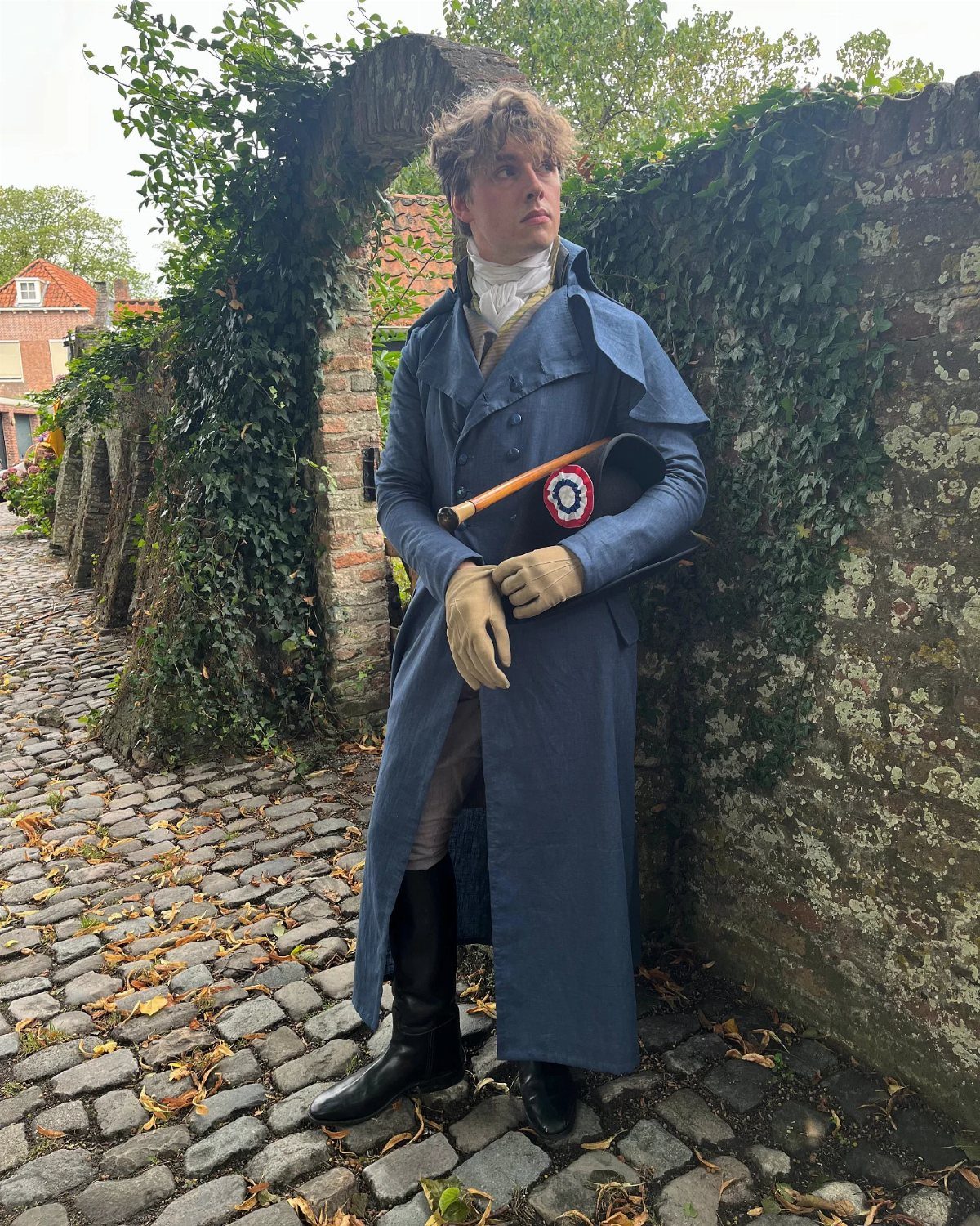 Man in blue Regency overcoat and cravat standing on a cobblestone street