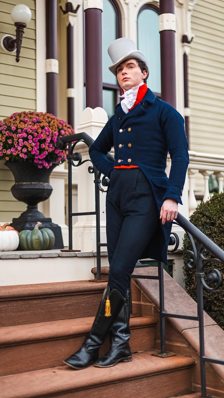 Man in navy regency tailcoat, top hat, and riding boots standing on stairs.
