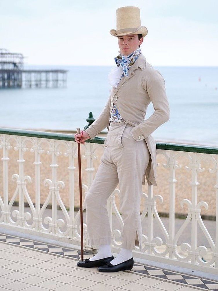 Man in beige Regency fashion with top hat and cane by the seaside