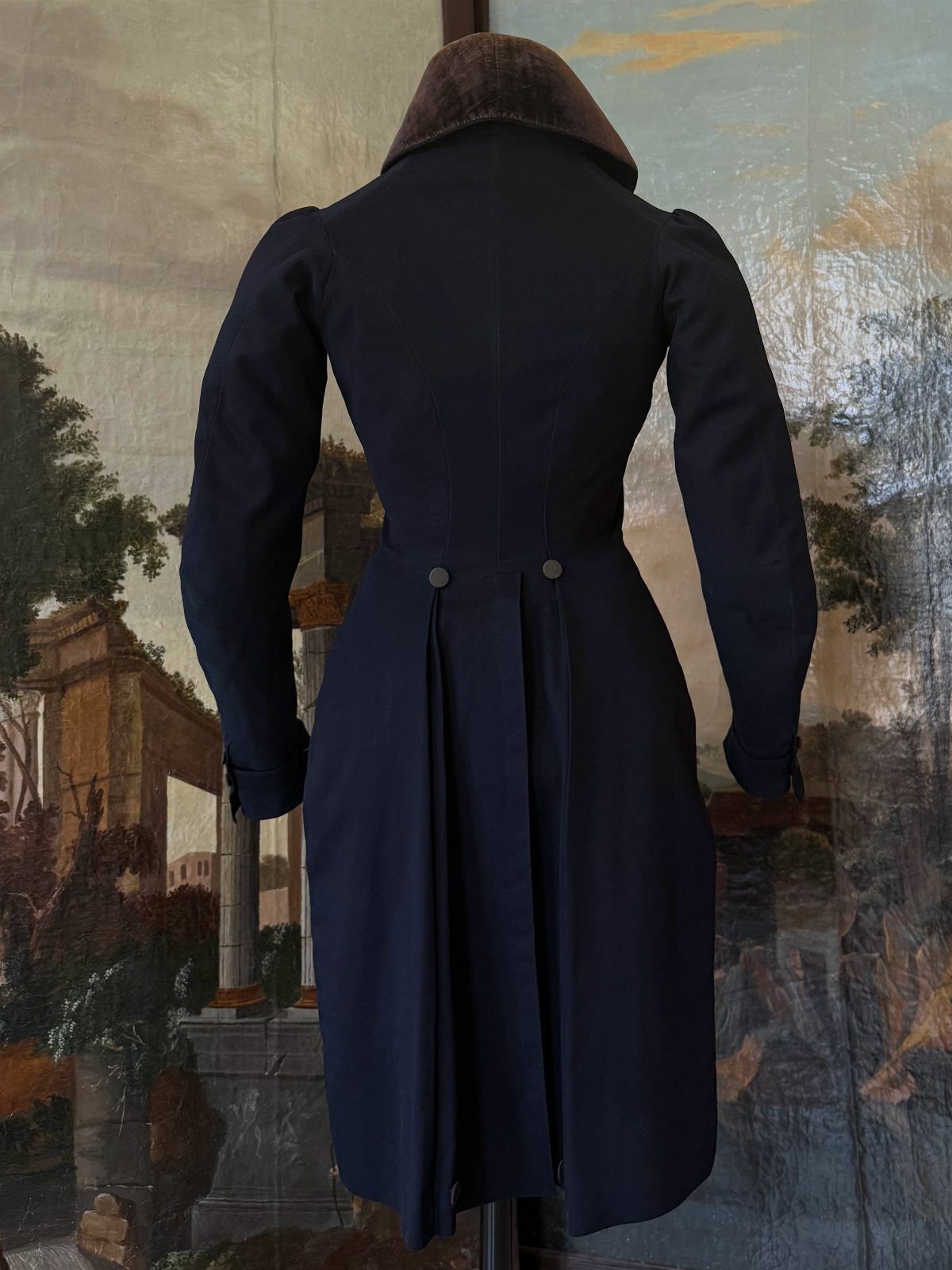 Dark blue Regency tailcoat with brown collar on a mannequin against landscape painting.