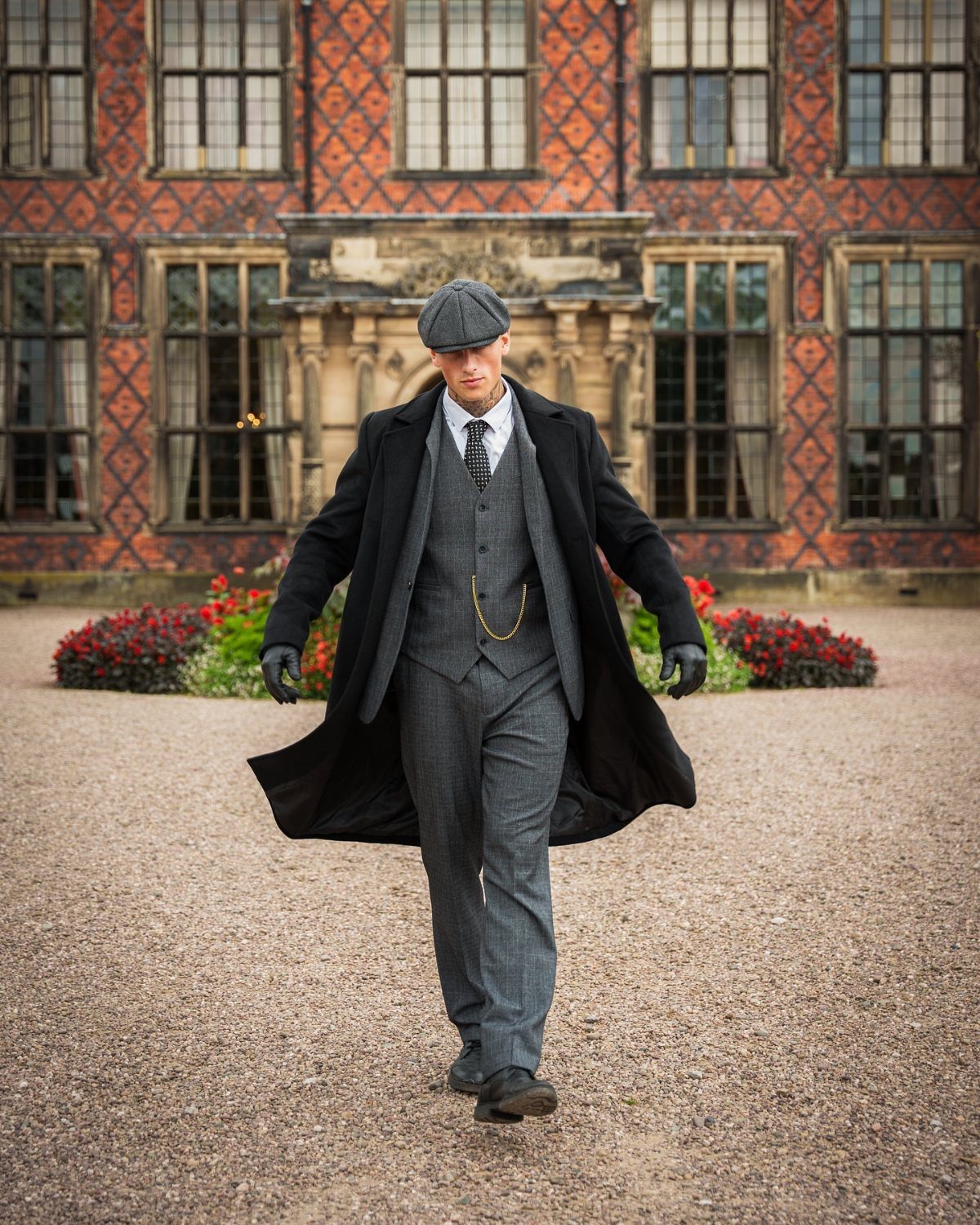 Man in a grey three-piece tailored suit and black overcoat walking outdoors.