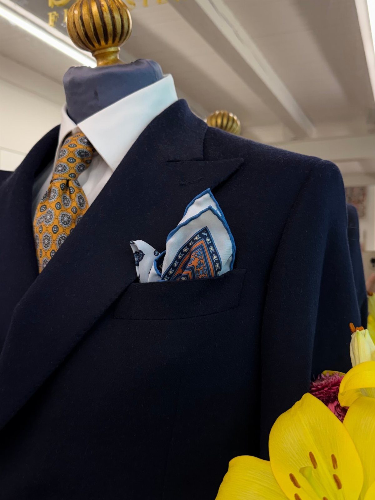 Navy blue suit jacket with a gold patterned tie and blue pocket square.