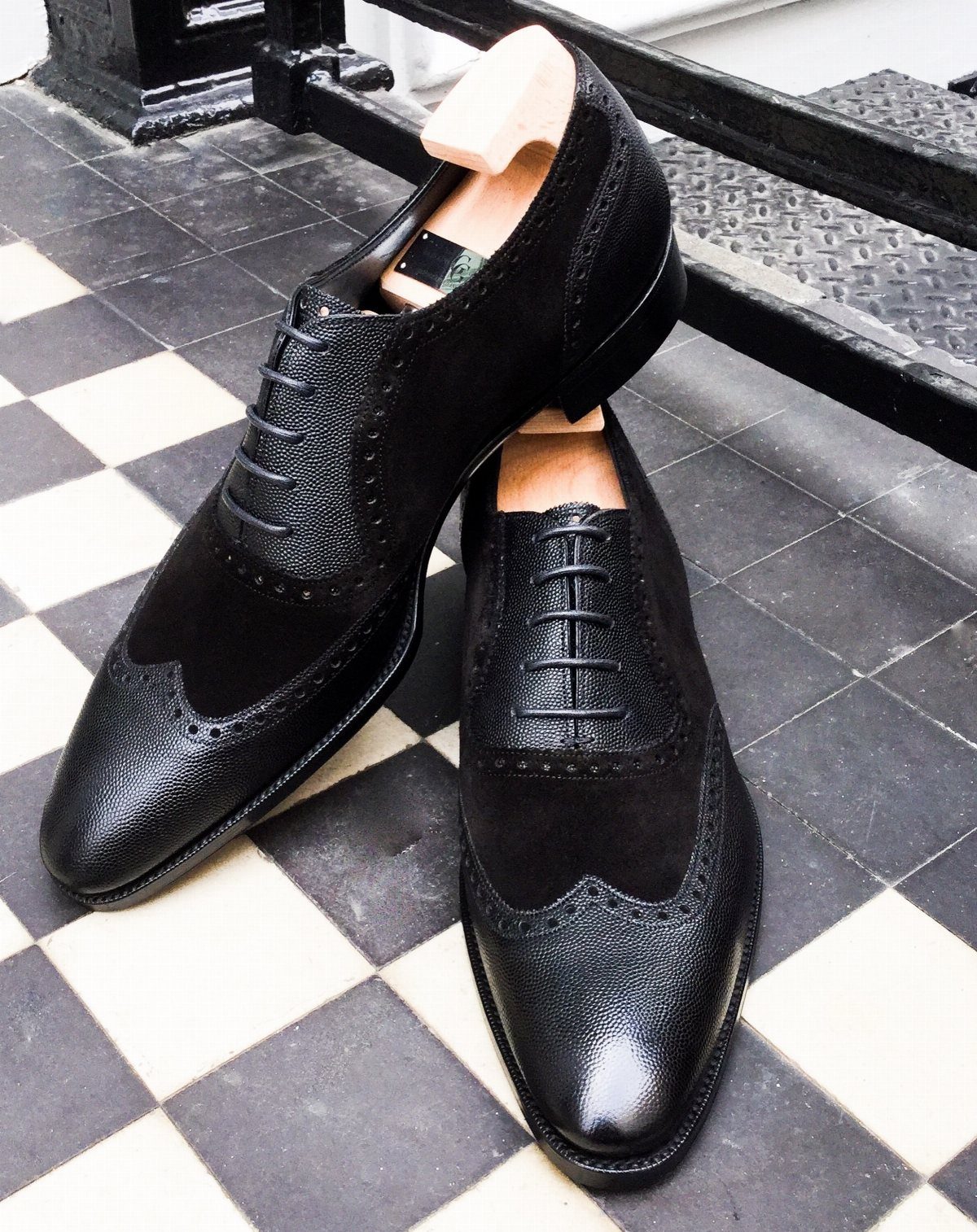 Black leather and suede wingtip oxford shoes on a checkered floor.
