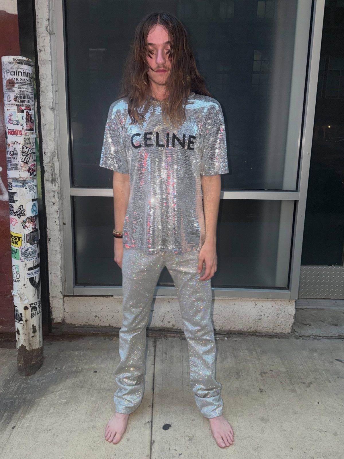 Man wearing a silver sequined t-shirt and matching sequined pants standing on a sidewalk.