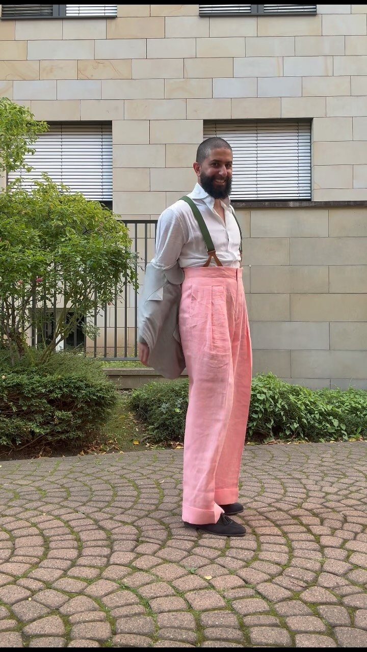 Man wearing high-waisted pink trousers and a white shirt on a cobblestone path.
