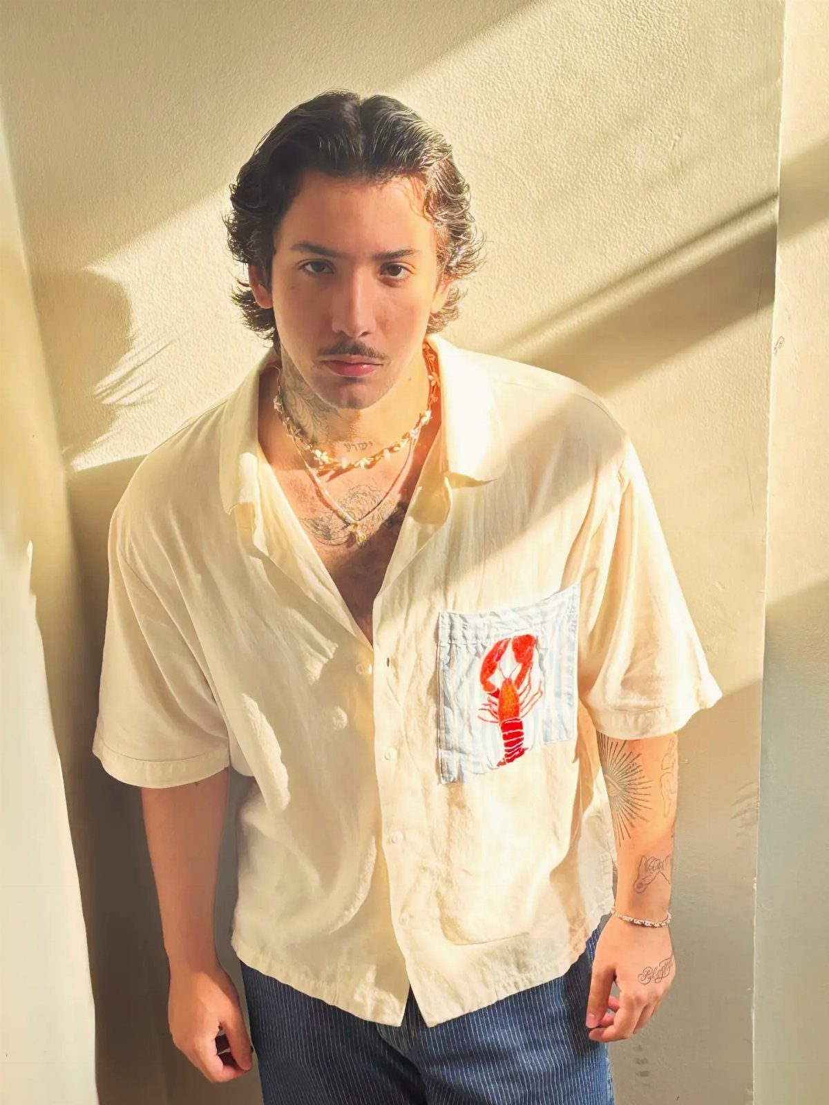 Man in a cream shirt with a red lobster graphic on the pocket.