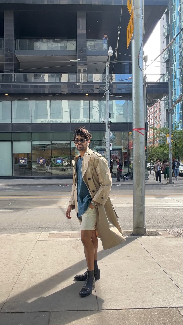 Man in a long tan trench coat and shorts on a city street.