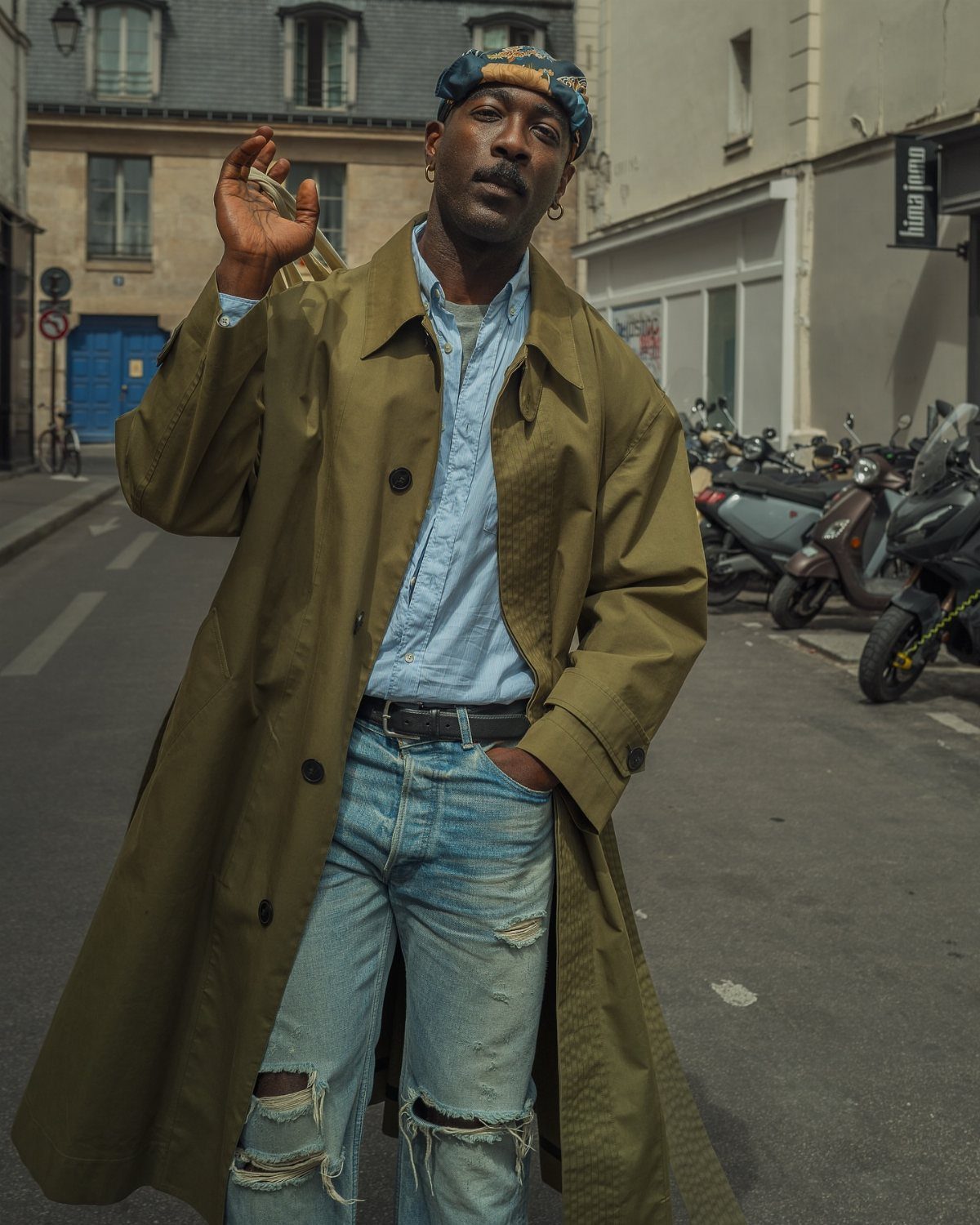 Man in olive green trench coat and distressed jeans on a city street.