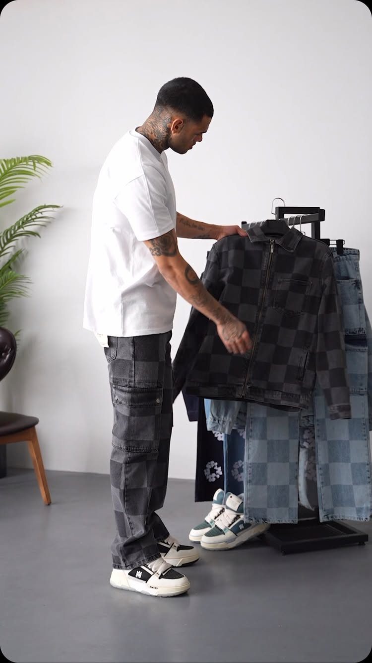 Man wearing checkered denim pants and holding a matching denim jacket.