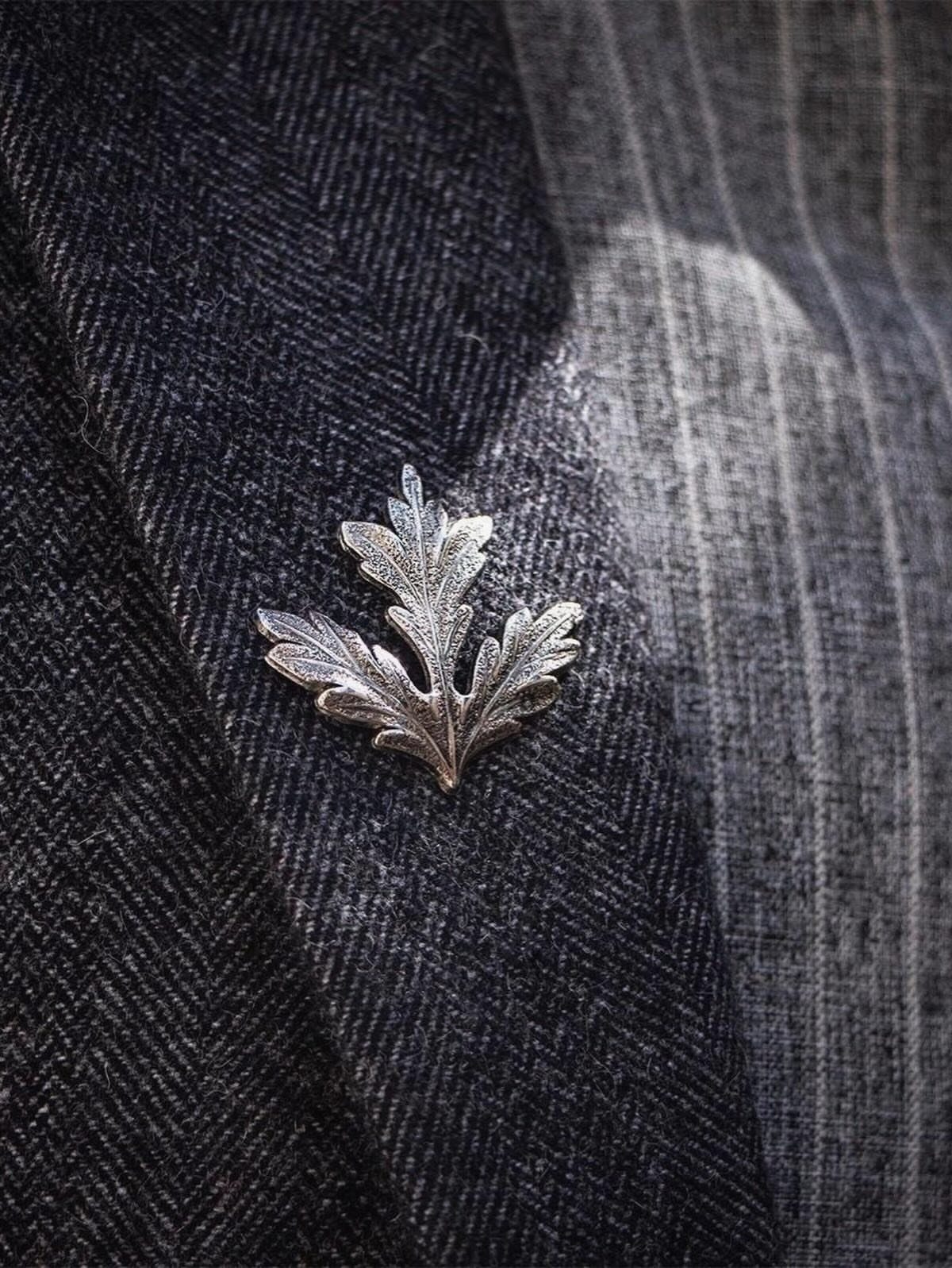 Silver leaf lapel pin on a dark grey herringbone blazer fabric