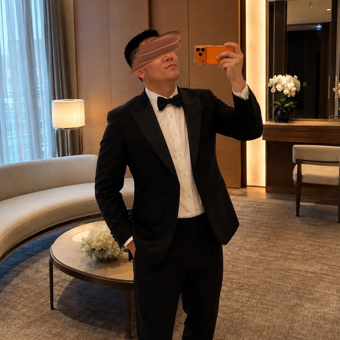 Man wearing a black tuxedo and bow tie taking a mirror selfie.