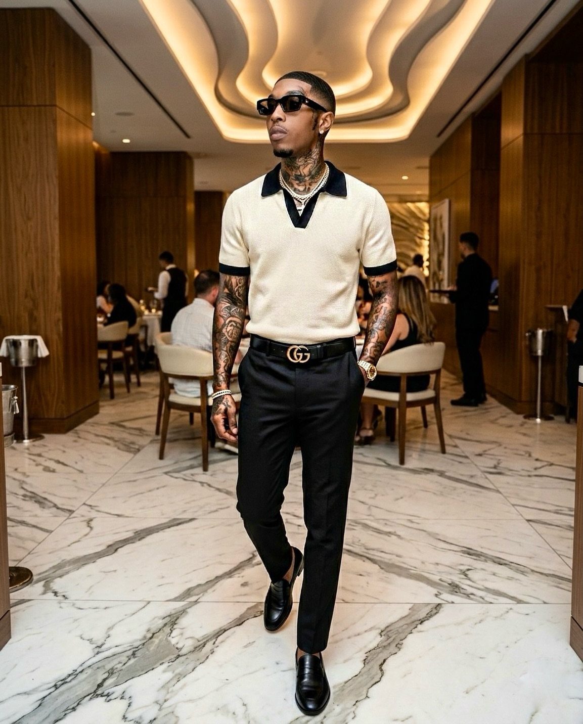 Man in a cream knit polo and black trousers walking in a luxury restaurant