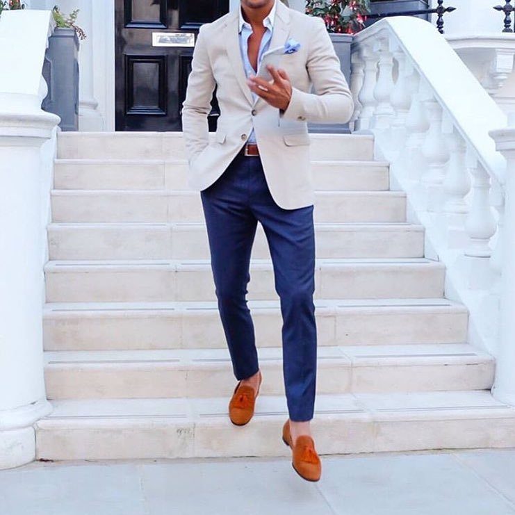 Man in beige blazer and navy trousers standing on white stone stairs.