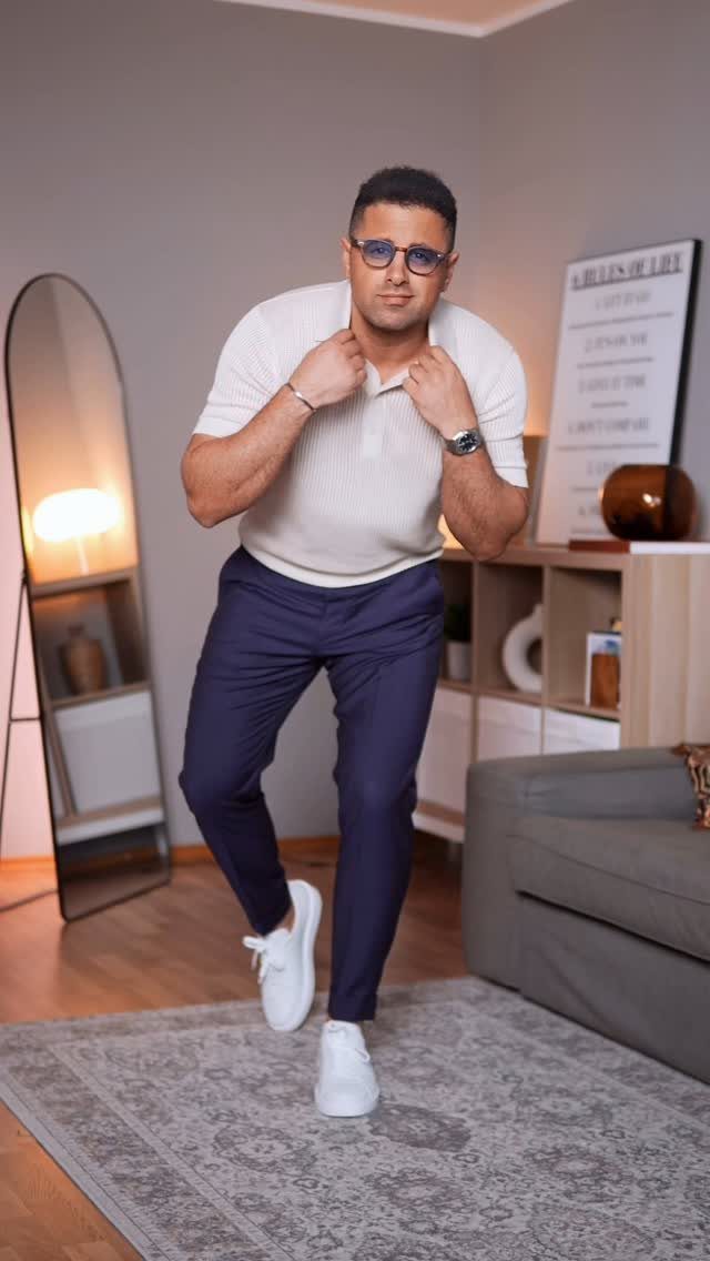 Man in white polo, navy trousers, and white sneakers posing in a living room.