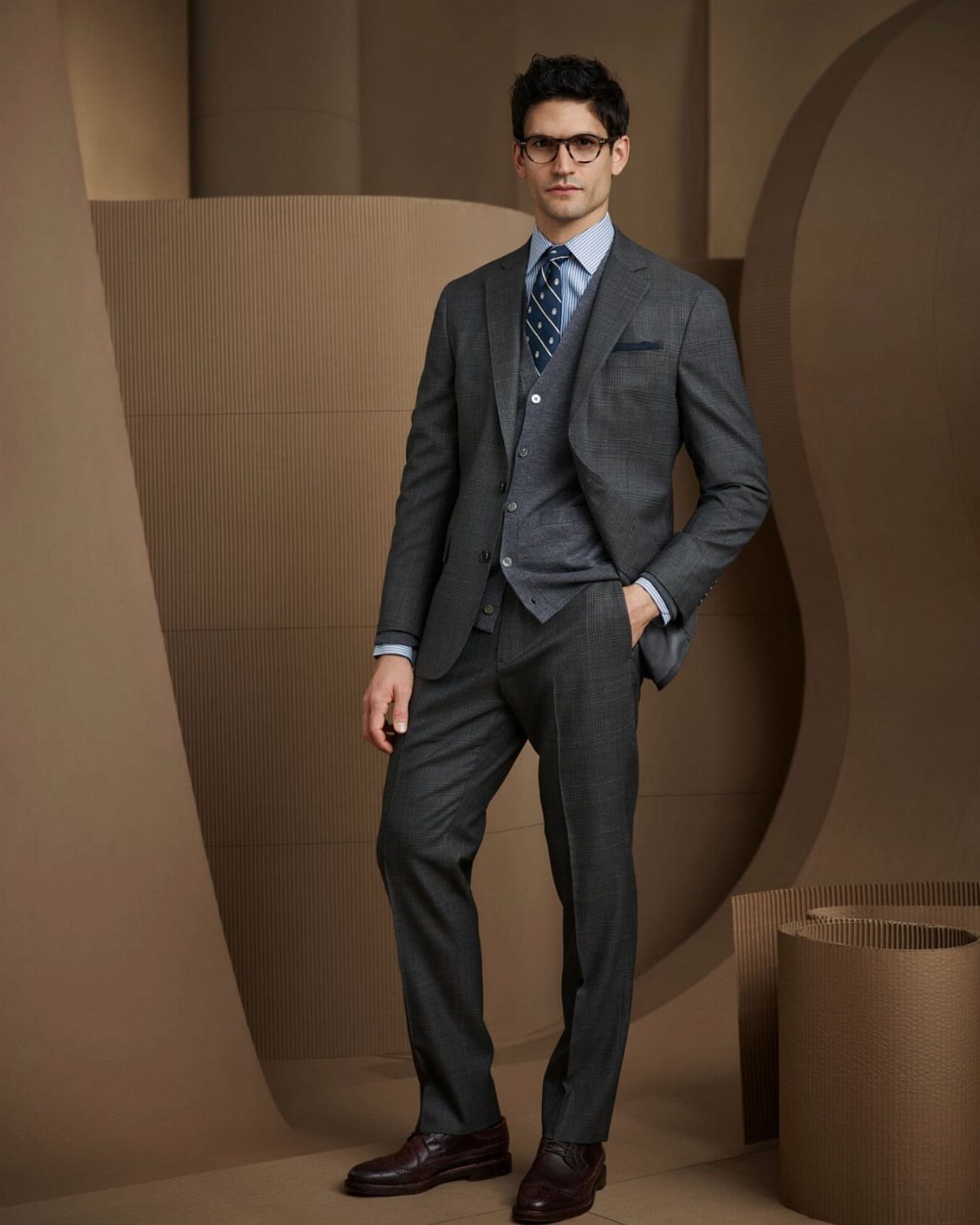 Man in a grey three-piece tailored suit with a blue tie and brown shoes.