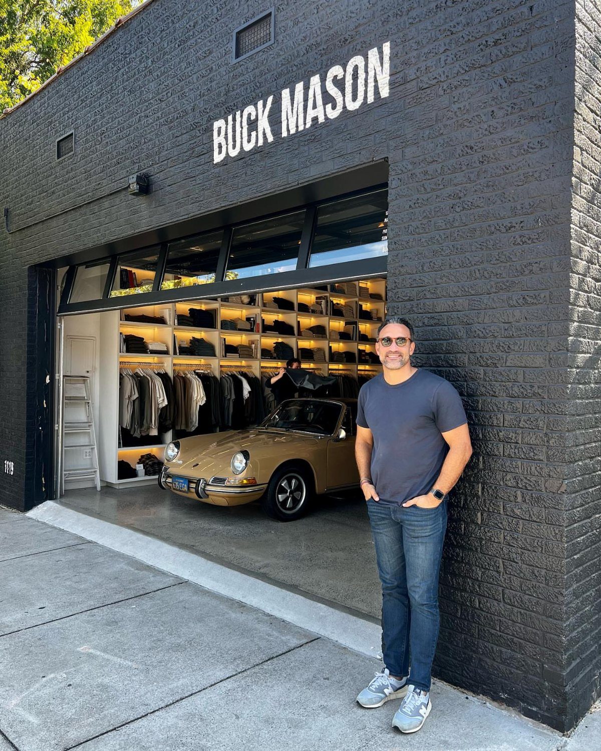 Man in grey tee and jeans posing outside a Buck Mason clothing store
