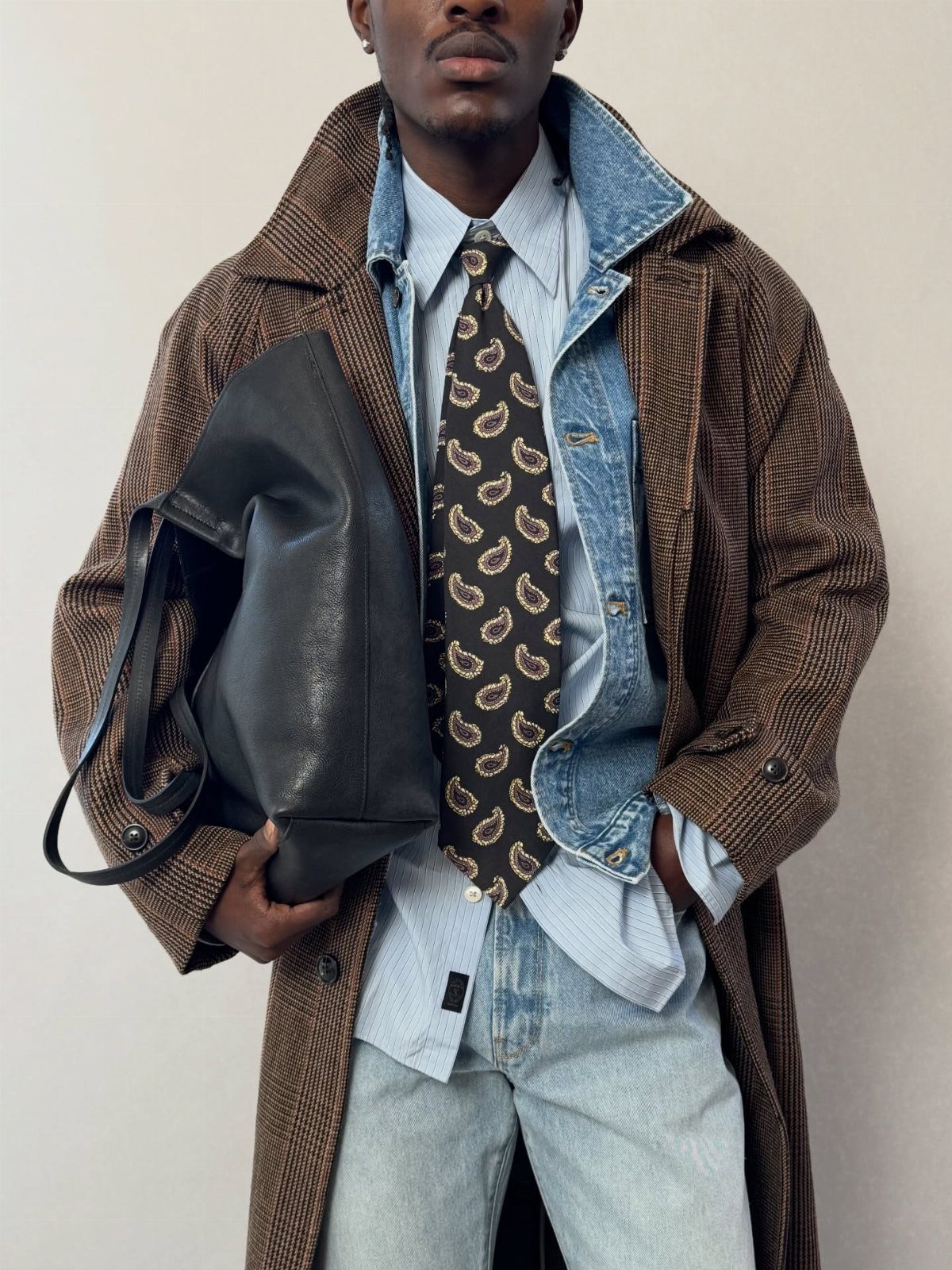 Man in a brown overcoat, denim shirt, paisley tie, and light-wash jeans.