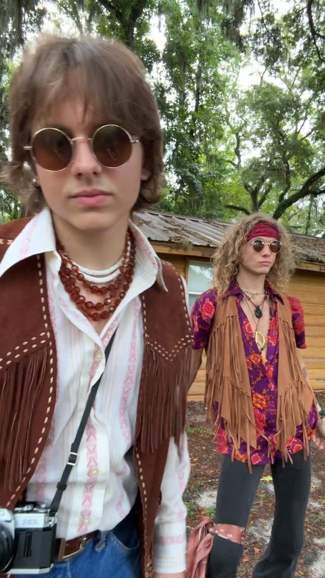 Two men wearing 1960s counterculture fashion with suede fringed vests and round sunglasses.