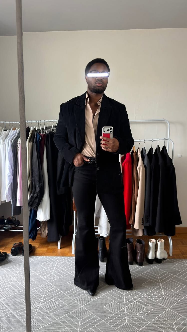 Man wearing black flared vintage pants, a tan shirt, and a black blazer.