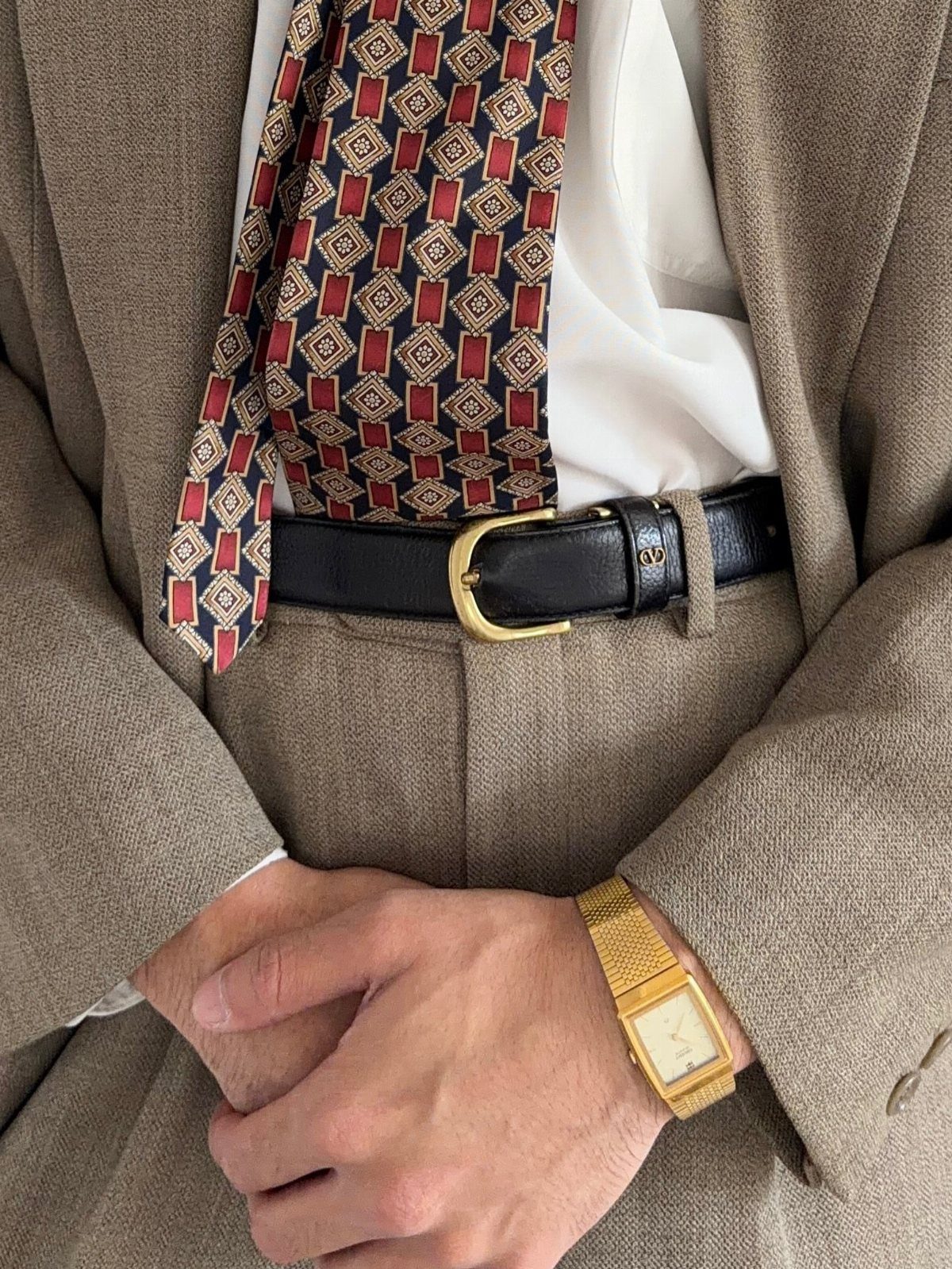Man wearing a gold watch, black leather belt, and patterned tie with brown suit.