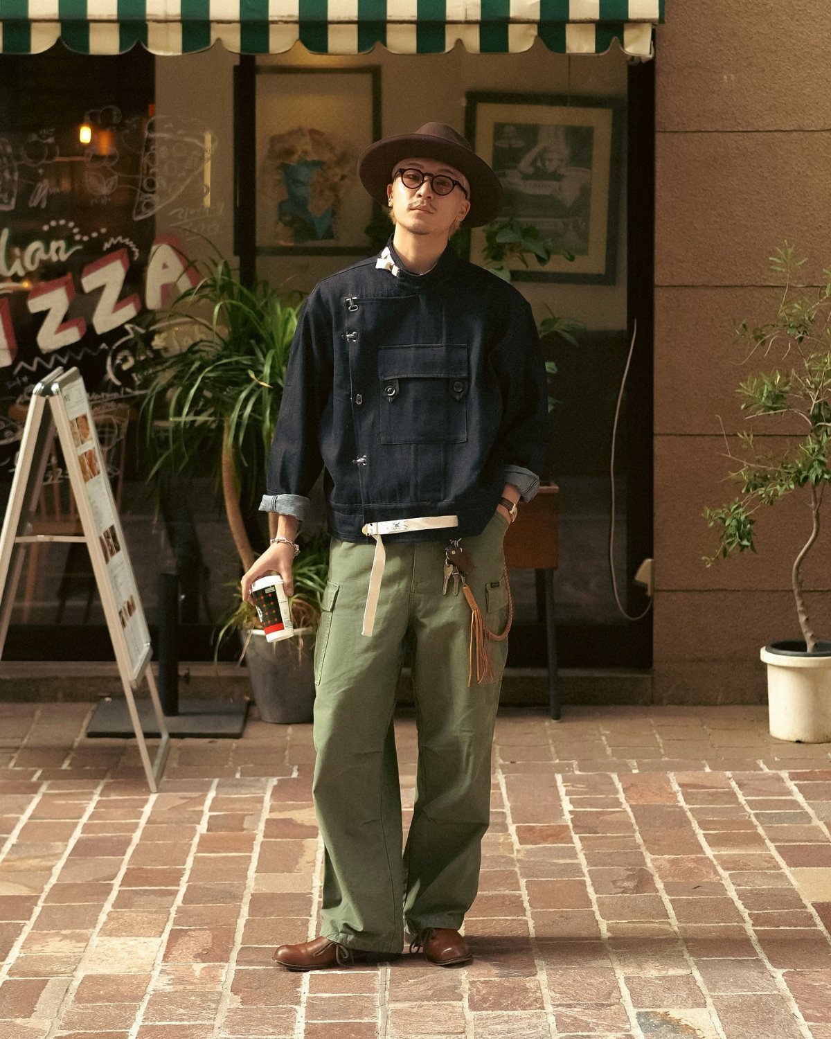 Man in vintage utility jacket, olive pants, and brown leather dress shoes standing outdoors.