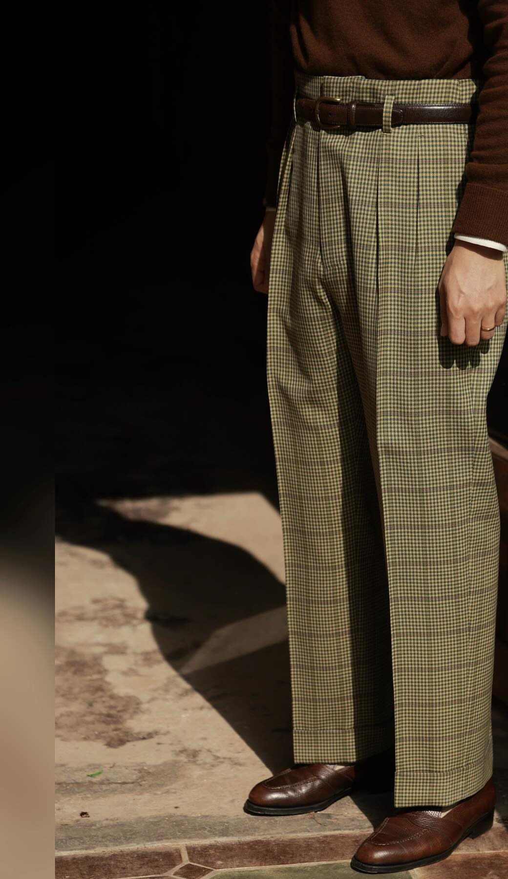 High-waisted pleated olive green plaid trousers with a brown leather belt and shoes.